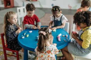 Six kindergarten children sit around a table playing with playdough