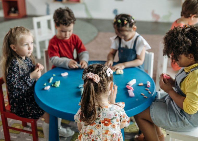 Six kindergarten children sit around a table playing with playdough