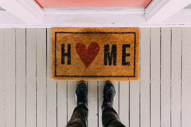 A door mat with the word home. The letter o has been replaced with a love heart.