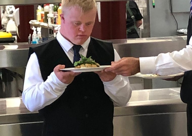 A young man working as a server receives instruction from a co-worker
