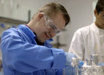 A young man with Down syndrome wearing a lab coat and working in a lab