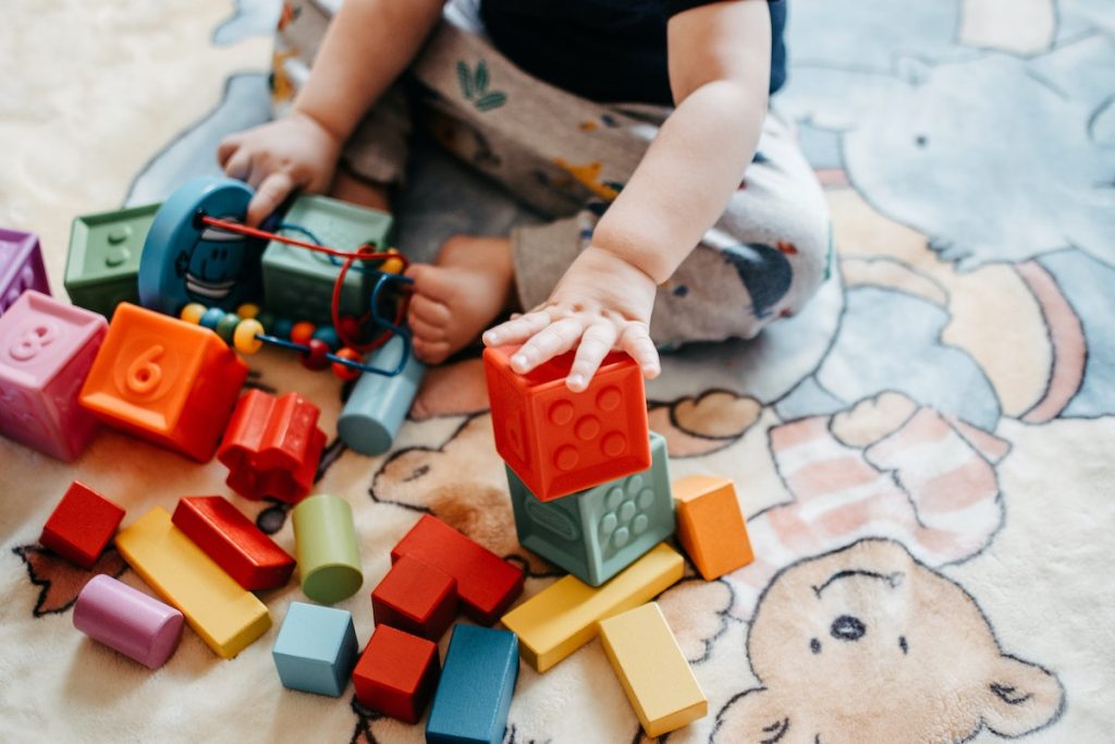 A small child sits on the floor playing with colourful building blocks