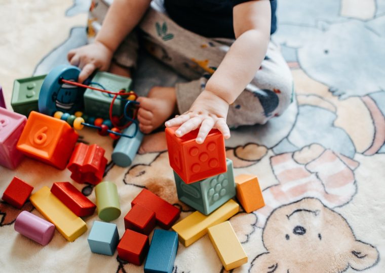 A small child sits on the floor playing with colourful building blocks